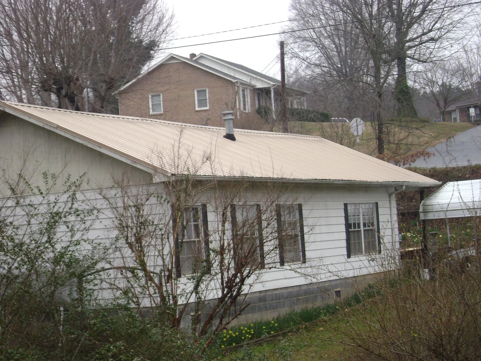 Tan metal roof on a white sided house set into a hillside — Commercial Roofing by Roofing Brothers in Hamilton