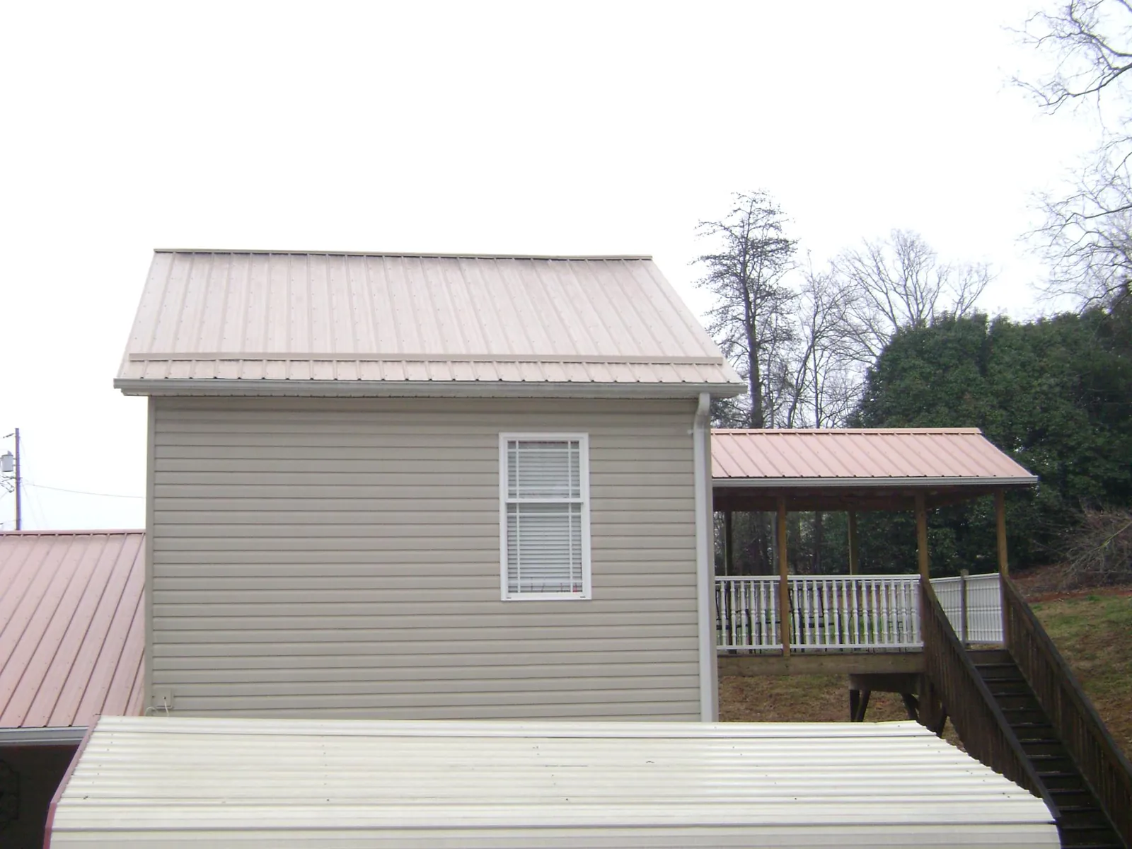 Tan metal roofs on a two story addition and attached porch, from a Roof Replacement job in Hamilton
